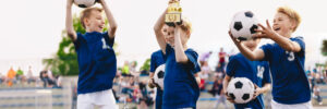 Happy boys in elementary school sports team celebrating soccer succes in tournament final game. Kids winning football game. Happy children sports team rising golden trophy